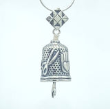 Handcrafted in sterling silver, the Quilting Hands Bell Pendant is shaped like a thimble. Pinking shears and the heart in hand symbol decorate the sides. A quilt block hangs above, forming the bail, and a seam ripper hangs below to ring the bell.