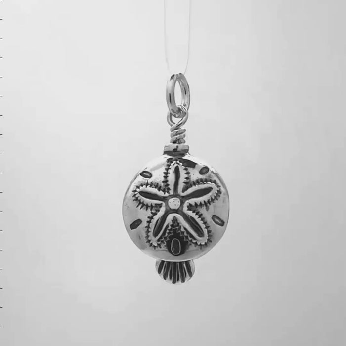In this video you can see our handcrafted sterling silver charm. The Sand Dollar Charm Bell is shaped like a sand dollar, with all its intricate patterns. A scallop shell hangs from the clapper, waiting to ring the bell.
